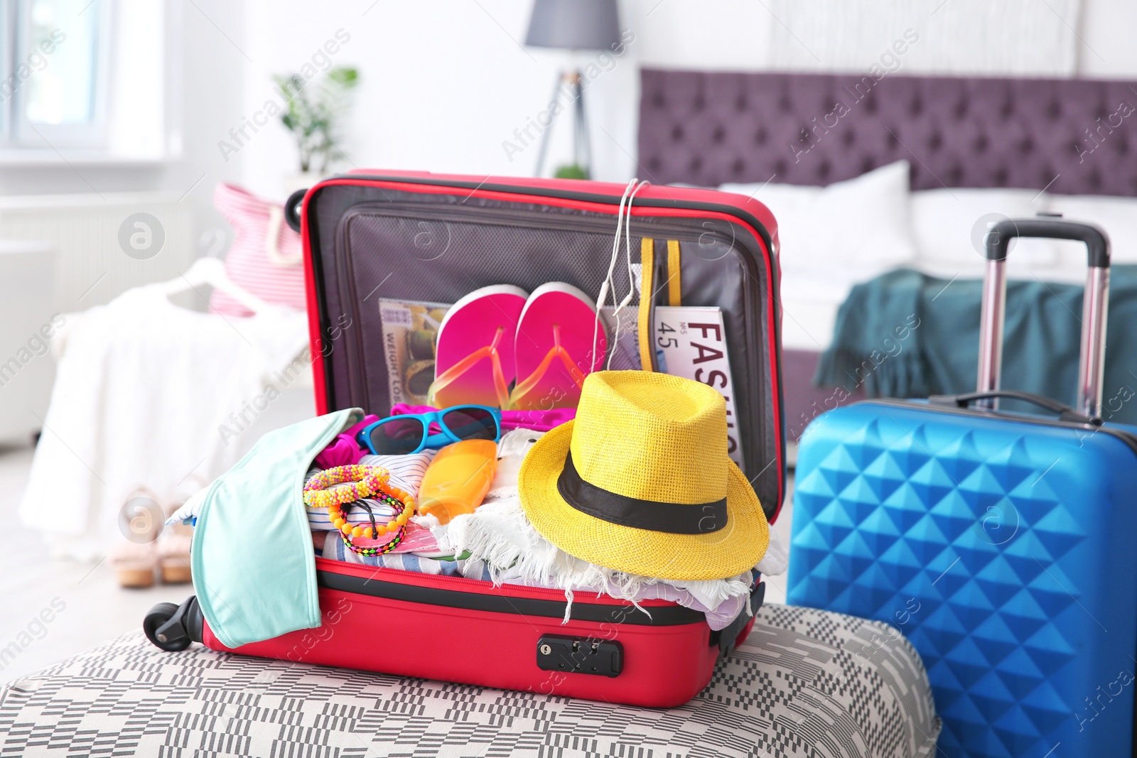 Photo of Open suitcase with different clothes and accessories for summer journey on ottoman chair