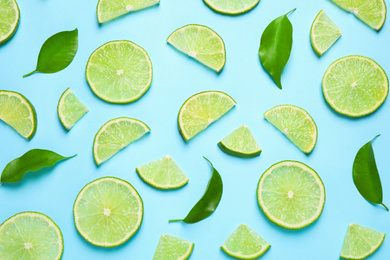 Juicy fresh lime slices and green leaves on light blue background, flat lay