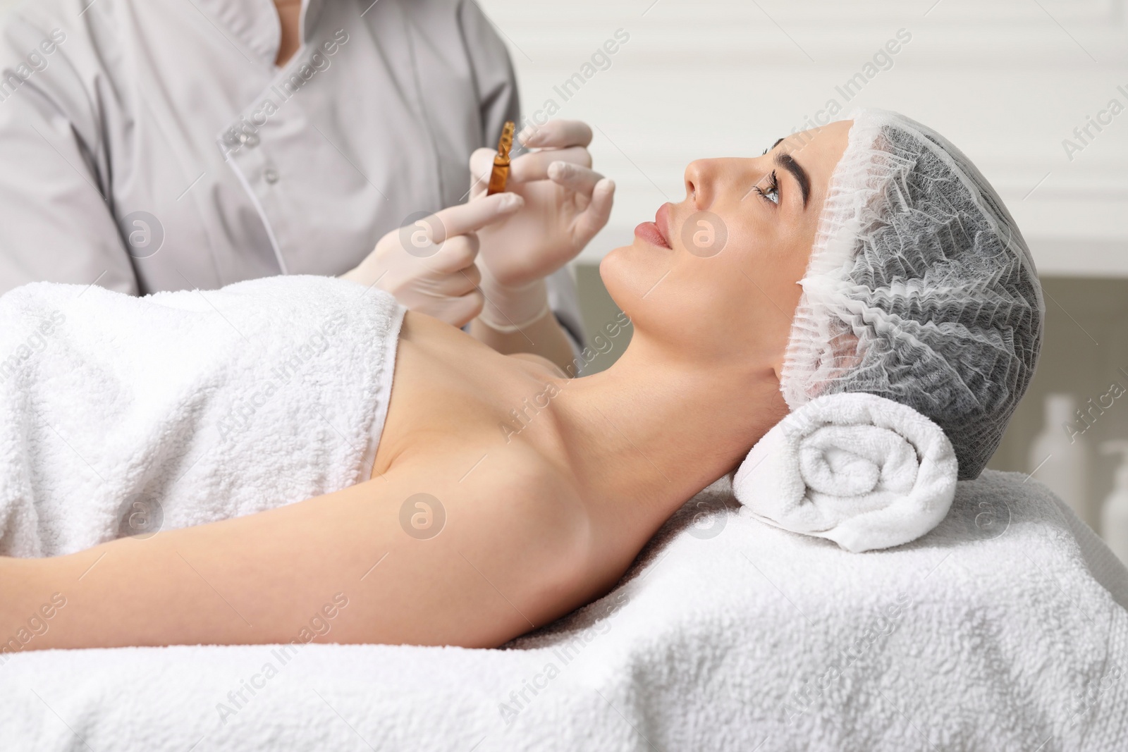 Photo of Professional cosmetologist holding skincare ampoule while working with client in clinic, closeup