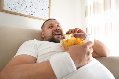 Photo of Lazy overweight man eating chips at home