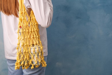 Photo of Woman with net bag full of different items near light blue wall, closeup and space for text. Conscious consumption