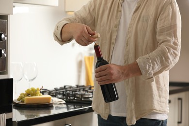 Man opening wine bottle with corkscrew indoors, closeup. Space for text