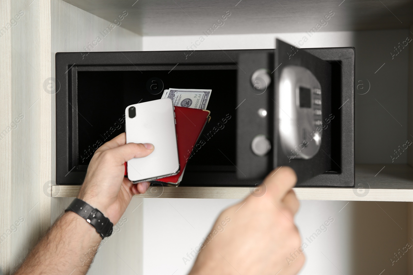 Photo of Man putting smartphone, passport and money into steel safe, closeup