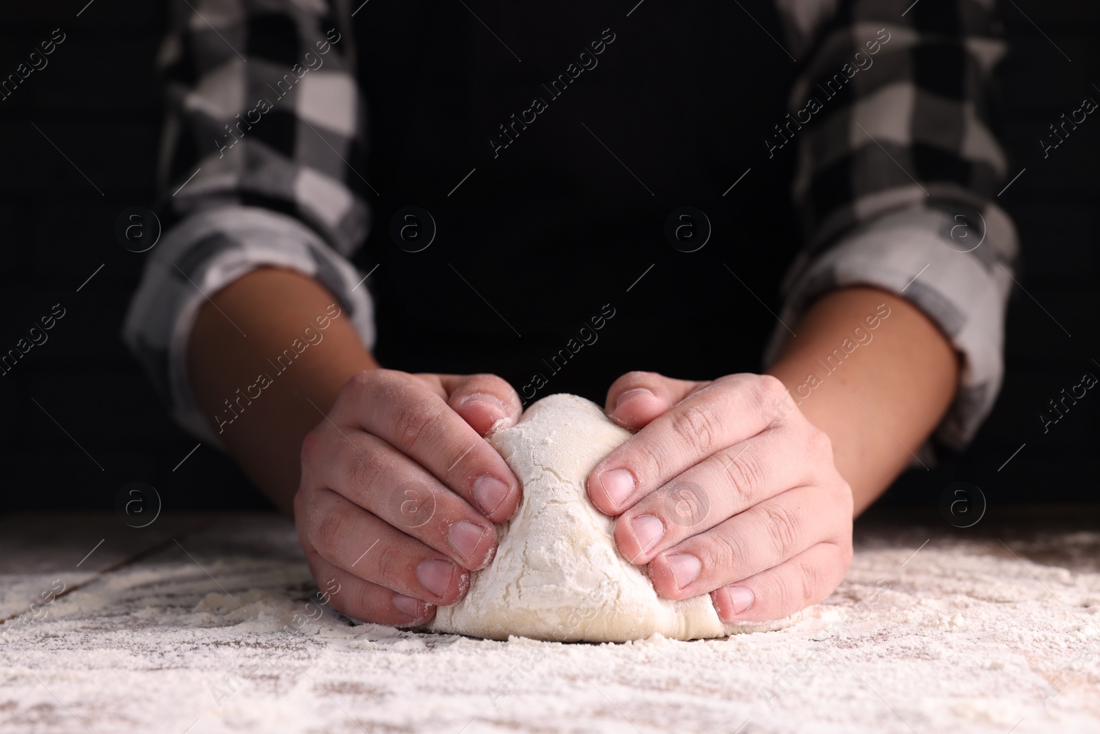 Photo of Man kneading dough at wooden table on dark background, closeup