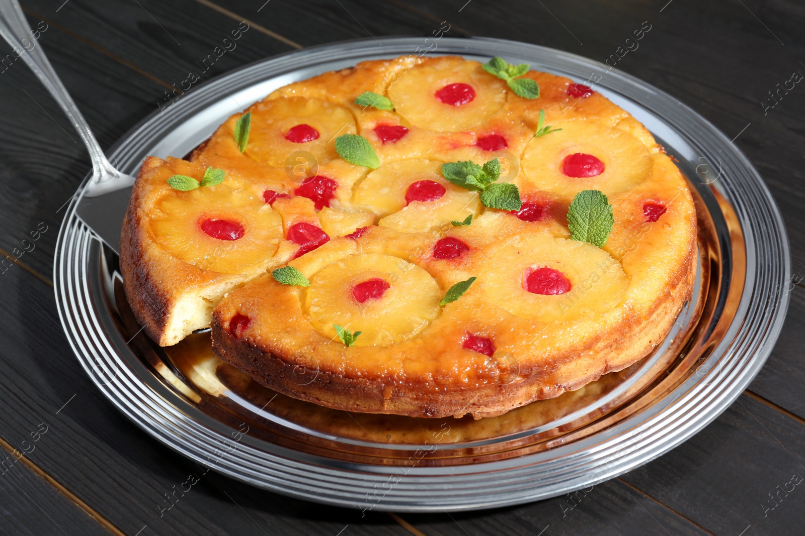 Photo of Taking piece of delicious cut pineapple pie with cherry and mint on dark wooden table