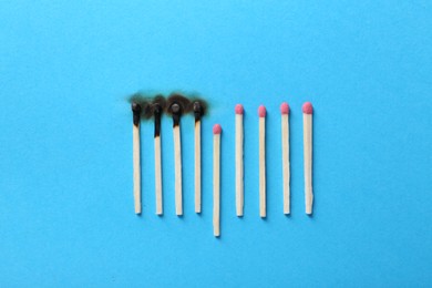 Burnt and whole matches on light blue background, flat lay. Stop destruction by breaking chain reaction concept