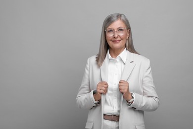 Portrait of beautiful senior woman in glasses on grey background. Space for text