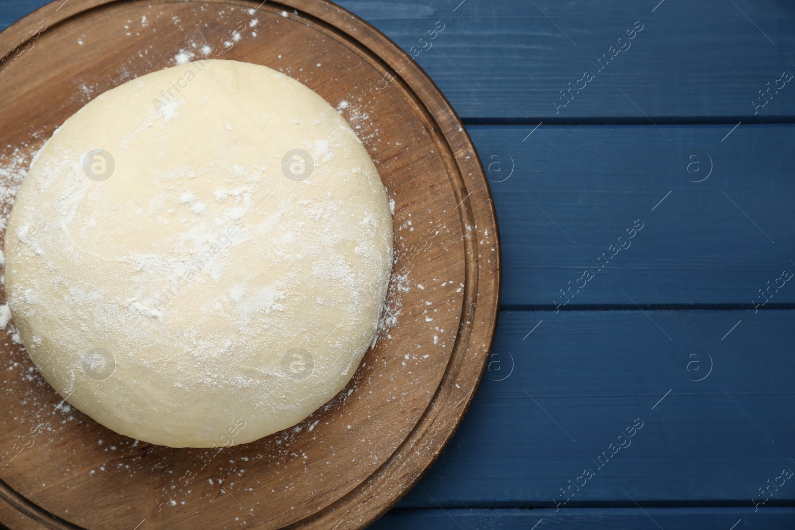 Photo of Fresh yeast dough with flour on blue wooden table, top view. Space for text