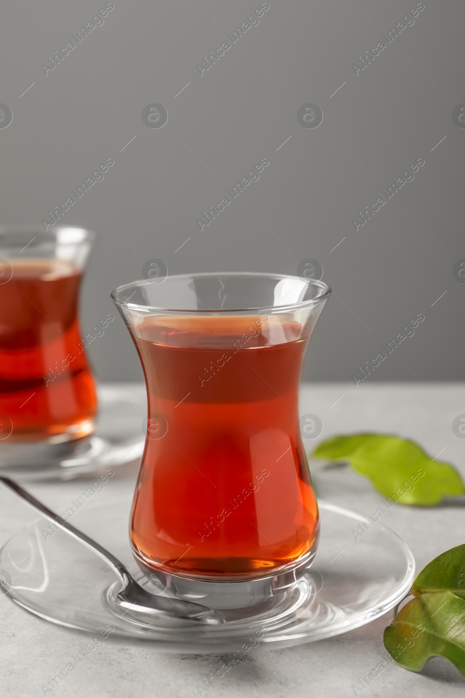 Photo of Glasses with traditional Turkish tea and green leaves on light grey table