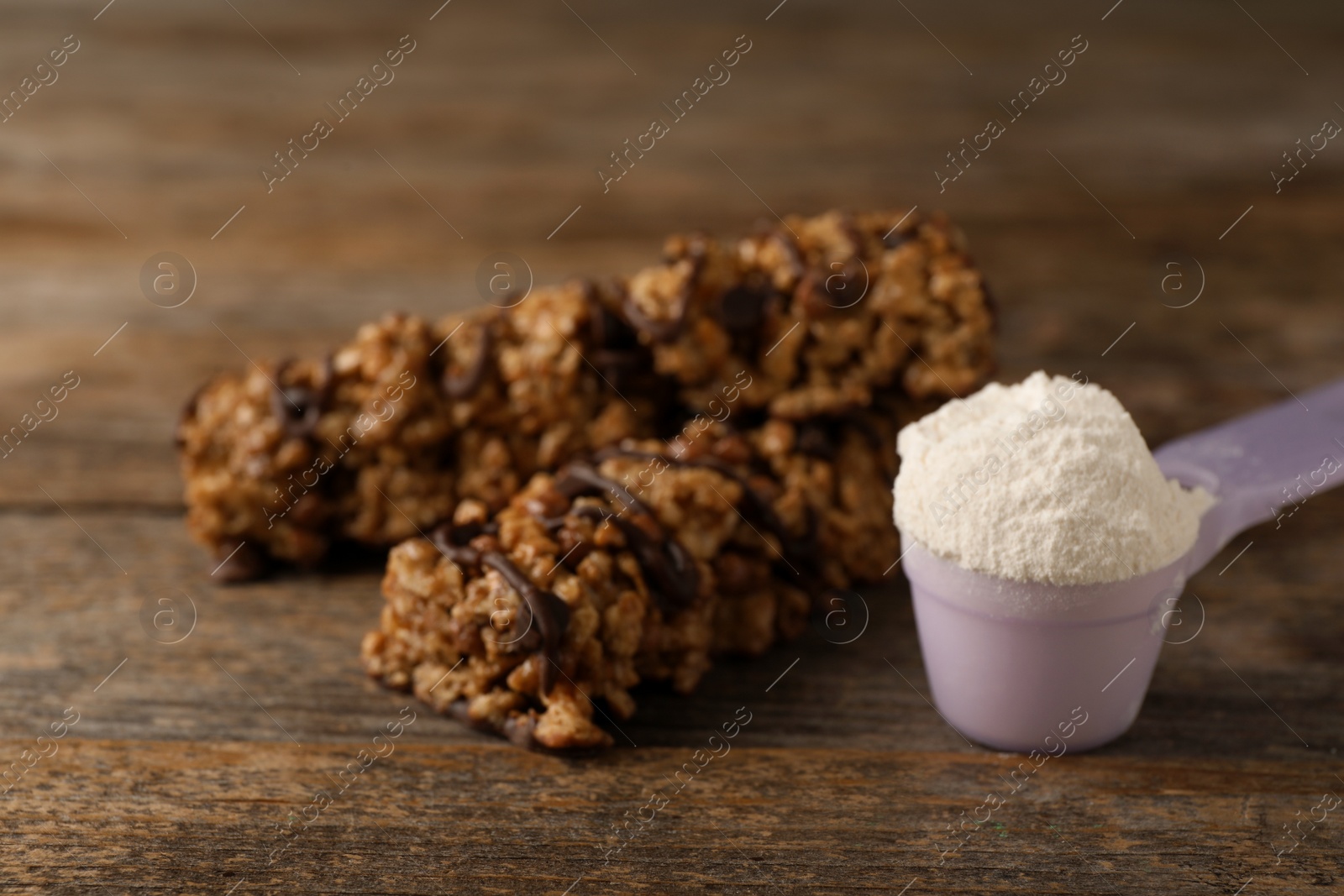 Photo of Tasty protein bars and scoop of powder on wooden table