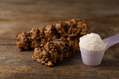 Tasty protein bars and scoop of powder on wooden table