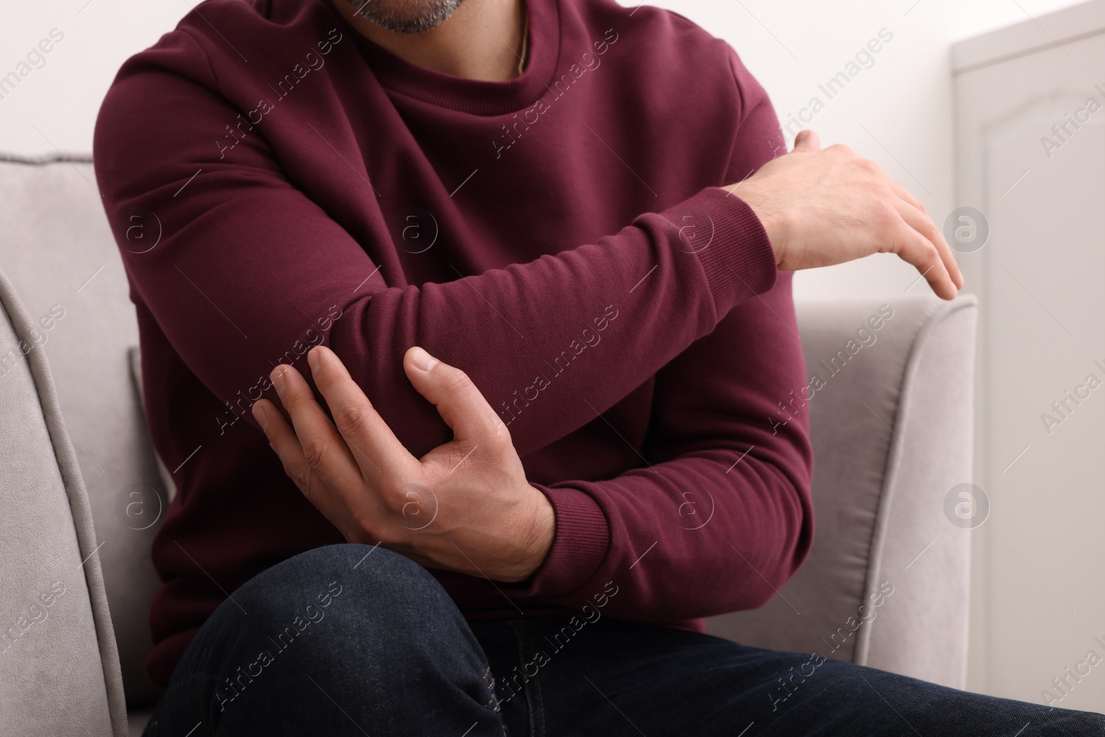 Photo of Man suffering from pain in his elbow on armchair indoors, closeup