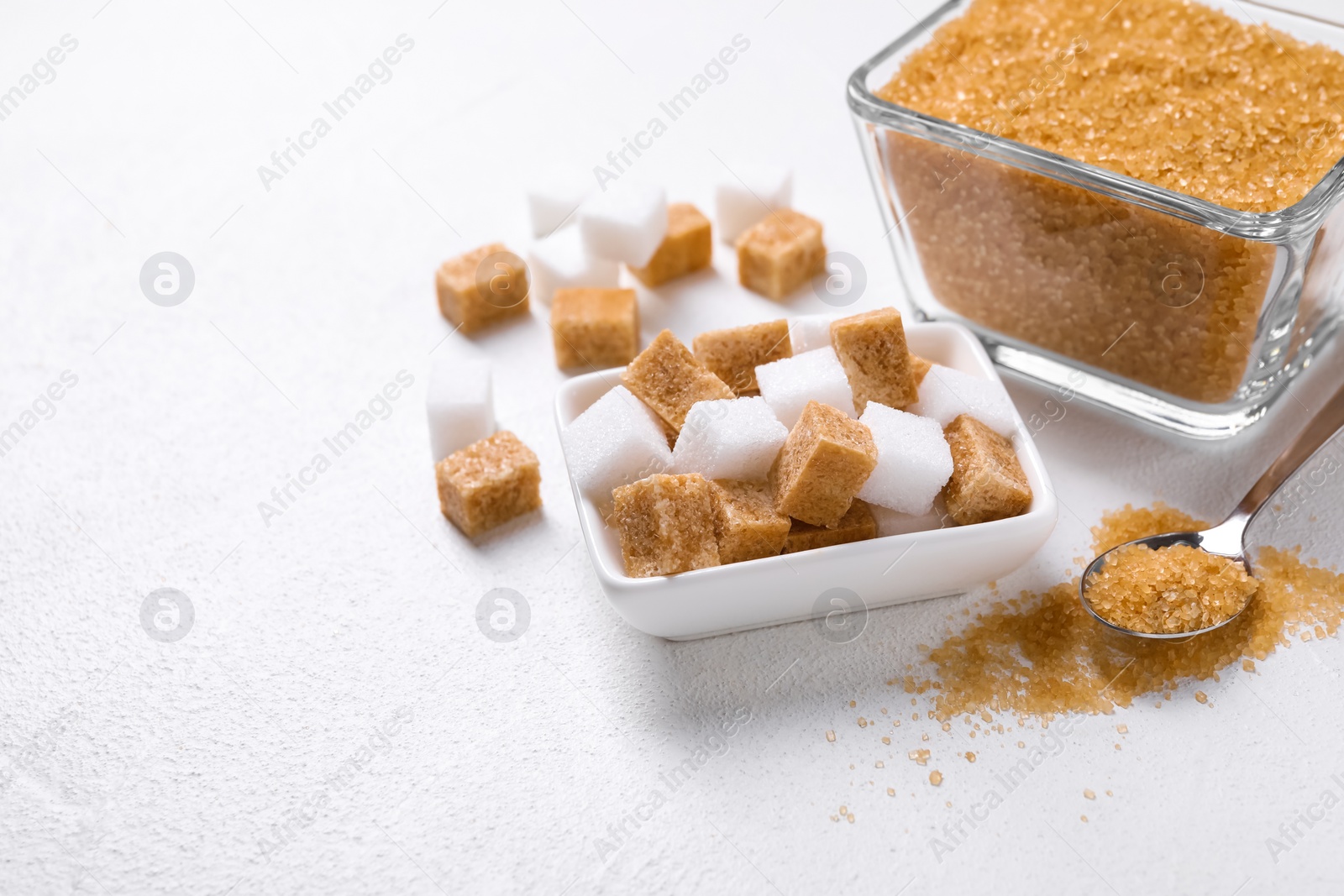 Photo of Bowls and spoon with different types of sugar on white table, closeup. Space for text