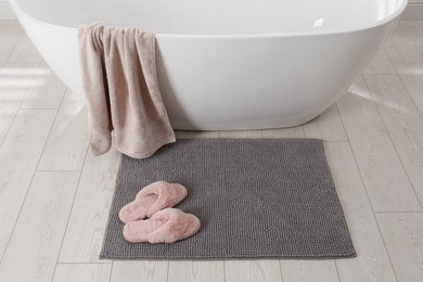 Photo of Soft grey bath mat and slippers on floor in bathroom