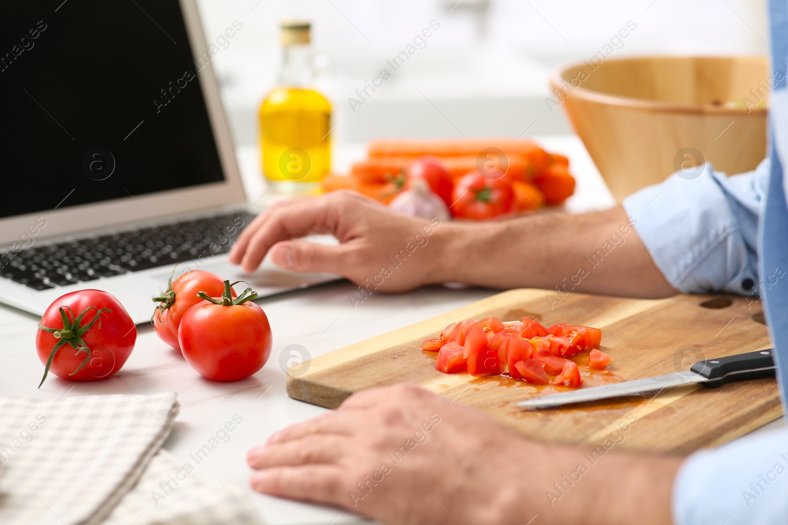 Photo of Man making dinner while watching online cooking course via laptop in kitchen, closeup