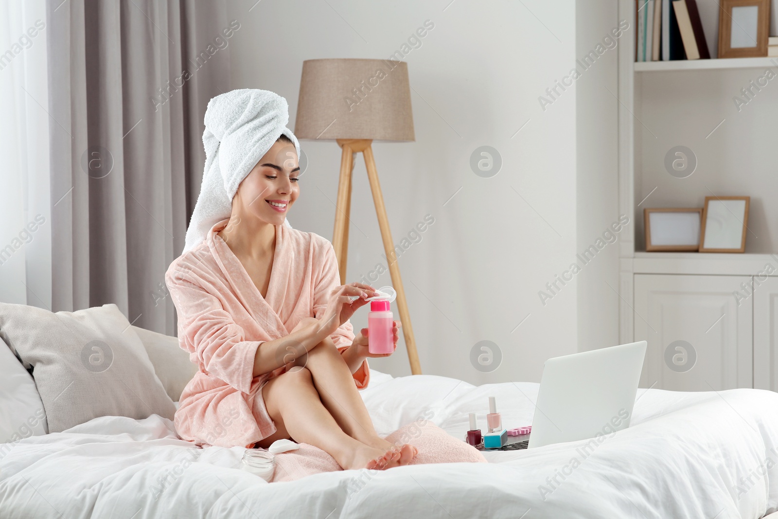 Photo of Beautiful young woman preparing toenails for pedicure on bed at home