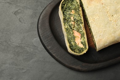 Photo of Delicious strudel with salmon and spinach on dark textured table, top view. Space for text
