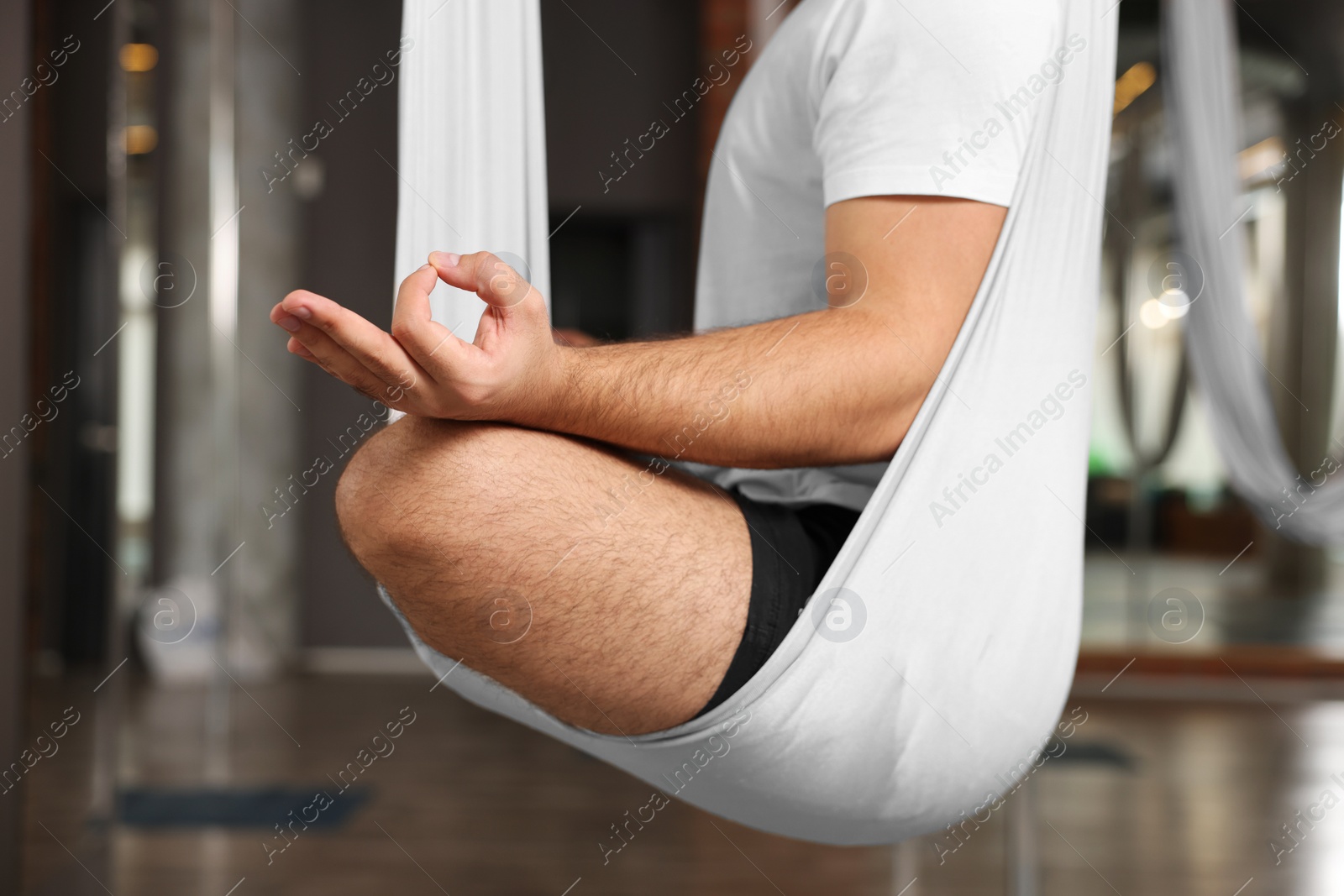 Photo of Man meditating in fly yoga hammock indoors, closeup