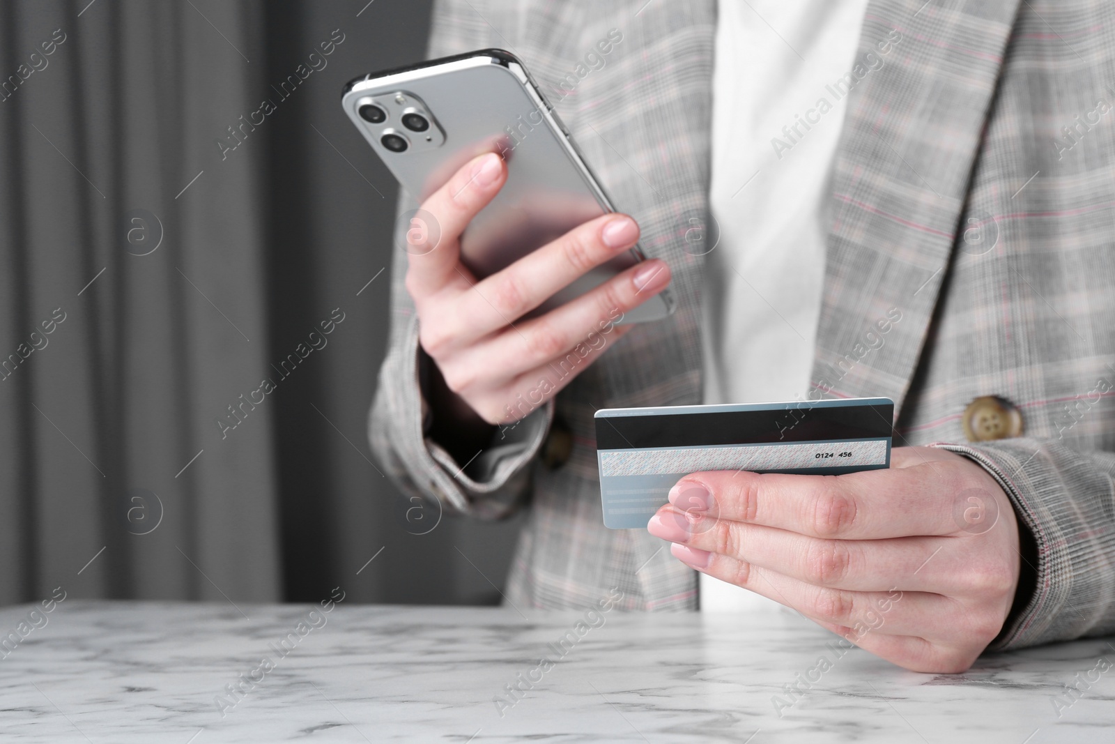 Photo of Online payment. Woman with smartphone and credit card at white marble table, closeup