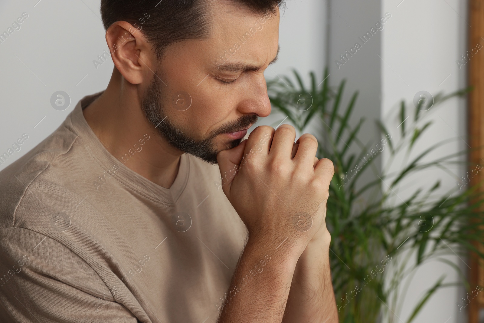 Photo of Man with clasped hands praying indoors, closeup