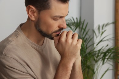 Man with clasped hands praying indoors, closeup