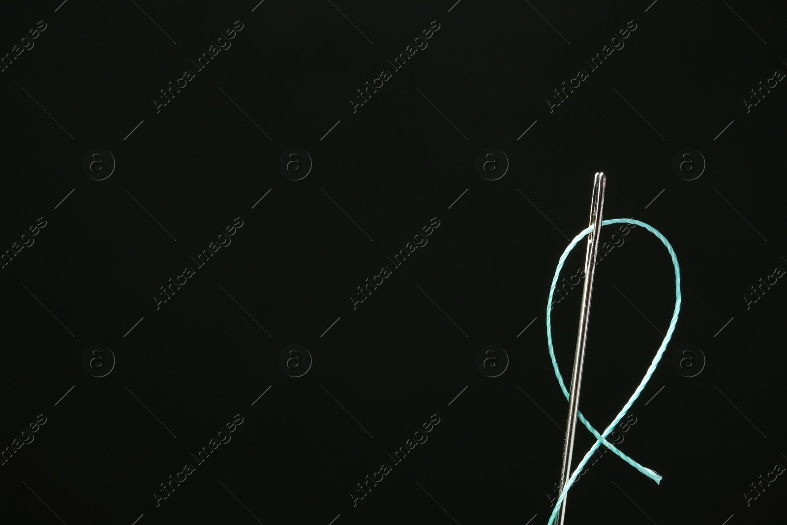 Photo of Needle with sewing thread on black background, closeup