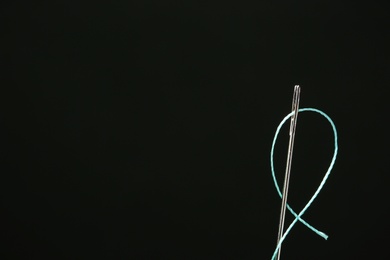 Photo of Needle with sewing thread on black background, closeup