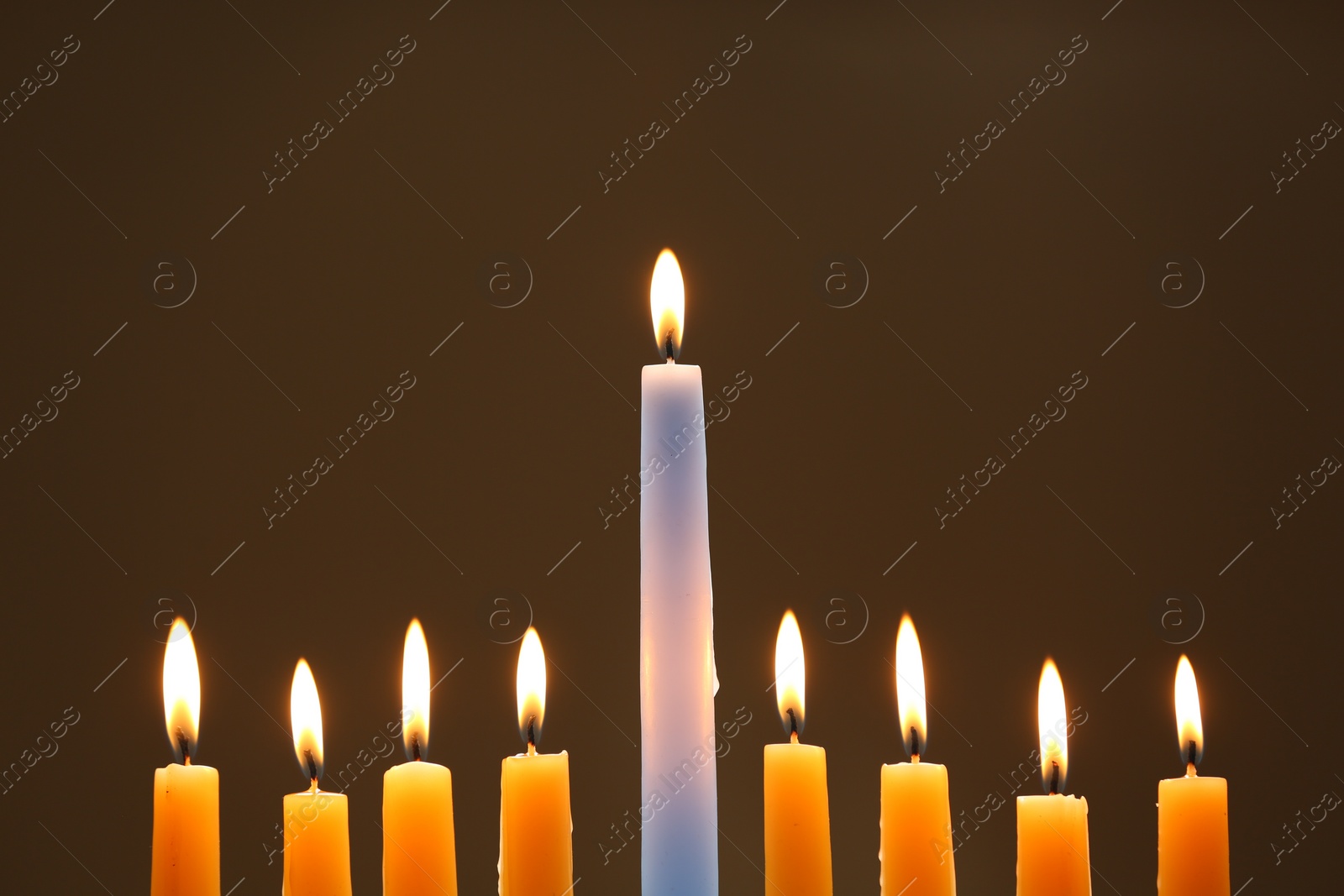 Photo of Hanukkah celebration. Burning candles on brown background, closeup