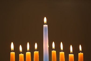 Hanukkah celebration. Burning candles on brown background, closeup