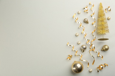 Shiny serpentine streamers, Christmas balls and decorative tree on light grey background, flat lay. Space for text