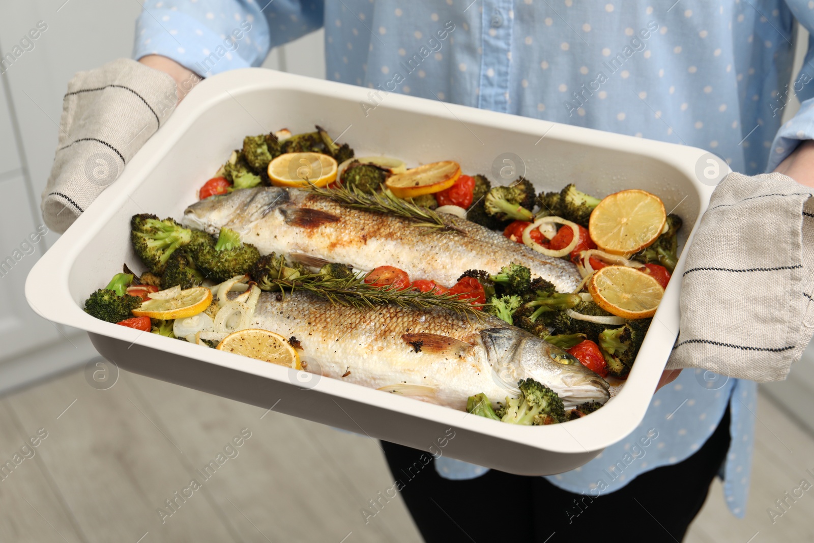 Photo of Woman holding baking dish with delicious fish and vegetables indoors, closeup