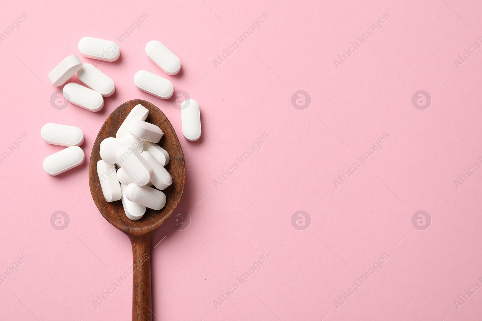 Photo of Vitamin capsules in wooden spoon on pink background, top view. Space for text