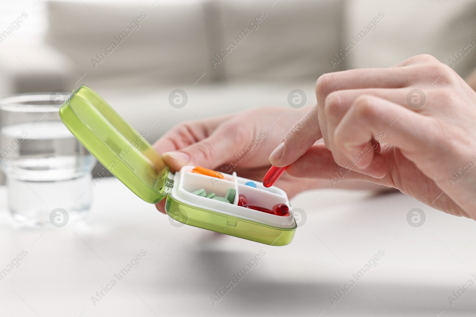 Photo of Woman with pills, organizer and glass of water at white table, closeup