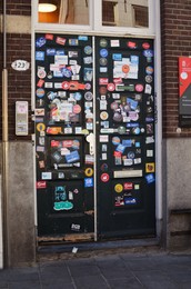 Photo of GRONINGEN, NETHERLANDS - APRIL 20, 2022: Door of modern building covered with different stickers outdoors
