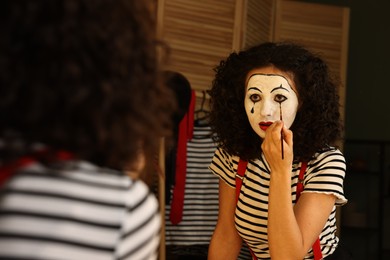 Photo of Young woman applying mime makeup near mirror indoors