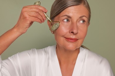 Woman massaging her face with jade roller on green background