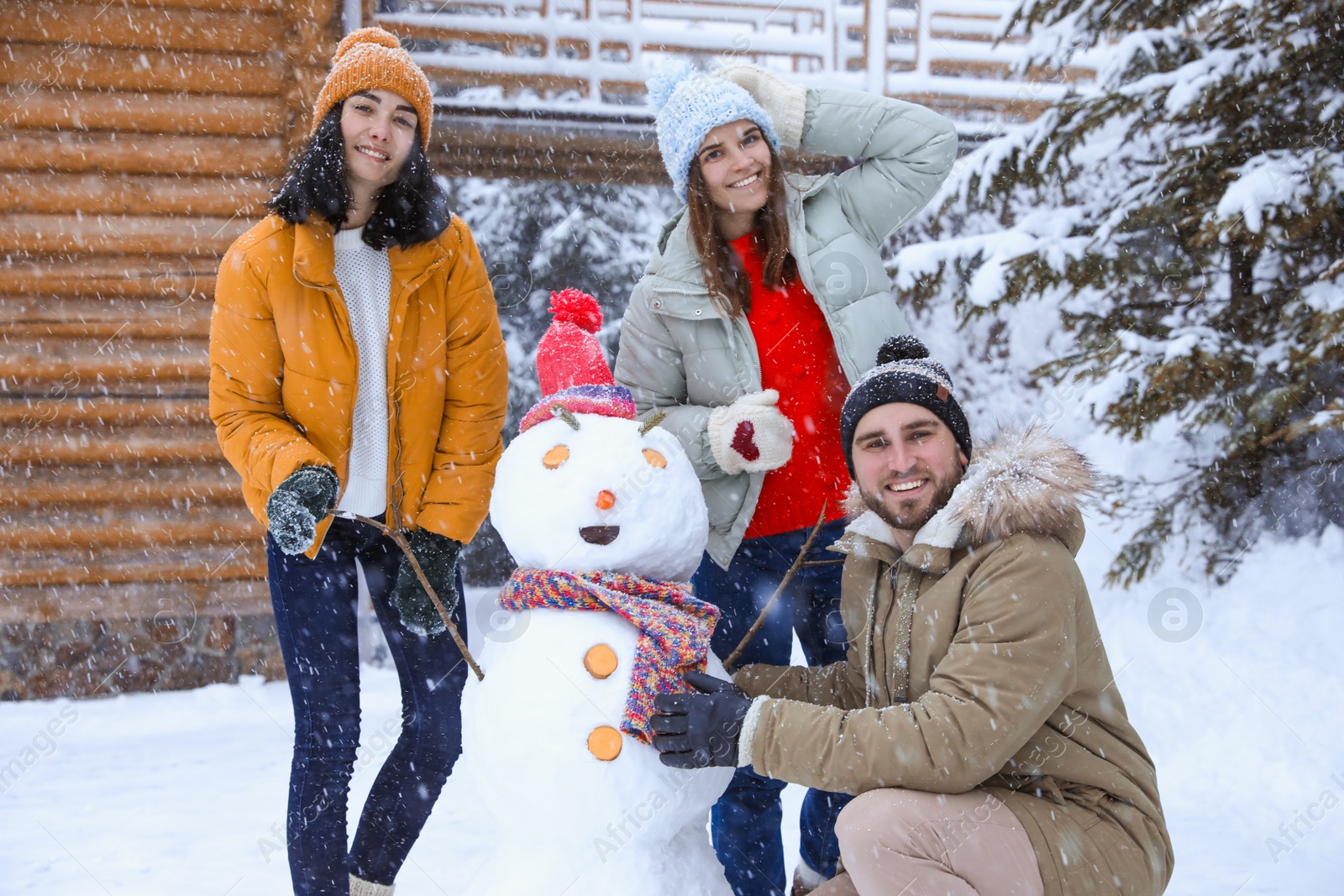 Photo of Happy friends with snowman outdoors on snowy day. Winter vacation