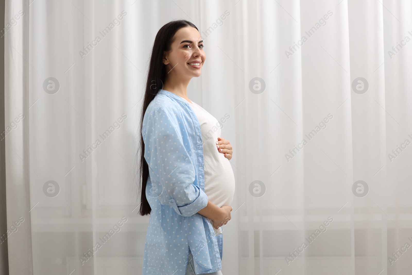 Photo of Happy pregnant woman near window indoors, space for text