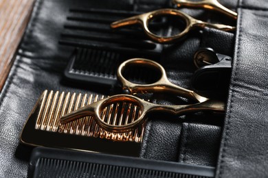 Photo of Hairdresser tools. Professional scissors and combs in leather organizer on wooden table, closeup