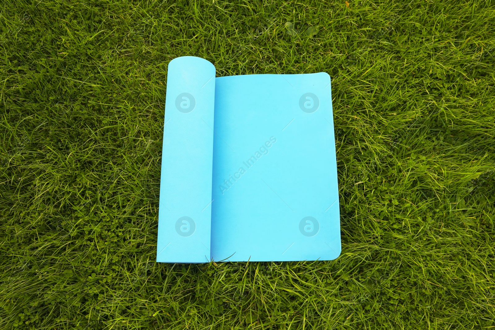 Photo of Blue karemat or fitness mat on fresh green grass outdoors, above view