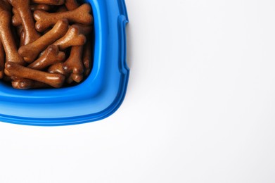 Blue bowl with bone shaped dog cookies on white background, top view. Space for text