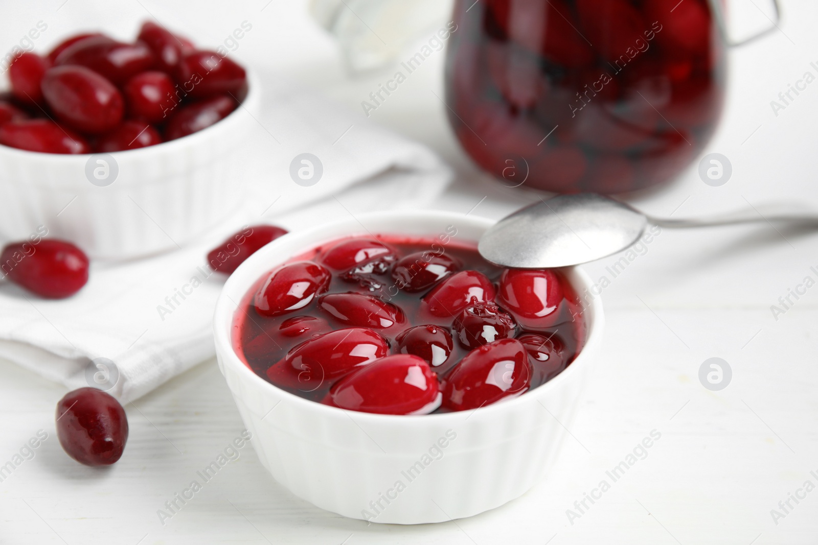 Photo of Delicious dogwood jam with berries and spoon on white wooden table, closeup