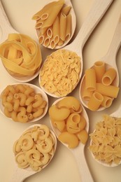 Different types of pasta in spoons on beige background, flat lay