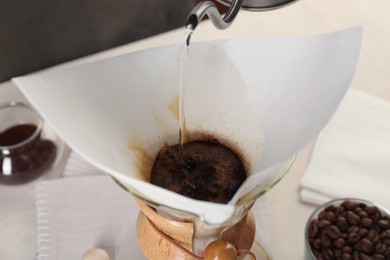 Photo of Making drip coffee. Pouring hot water into chemex coffeemaker with paper filter at table, closeup