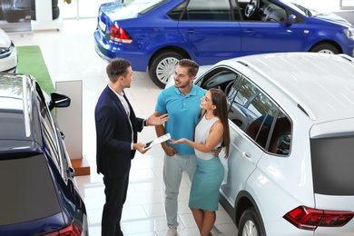 Salesman consulting young couple in car salon