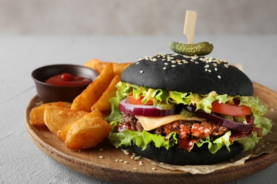 Photo of Wooden plate with black burger and french fries on table, closeup