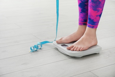 Photo of Woman with tape measuring her weight using scales on floor. Healthy diet