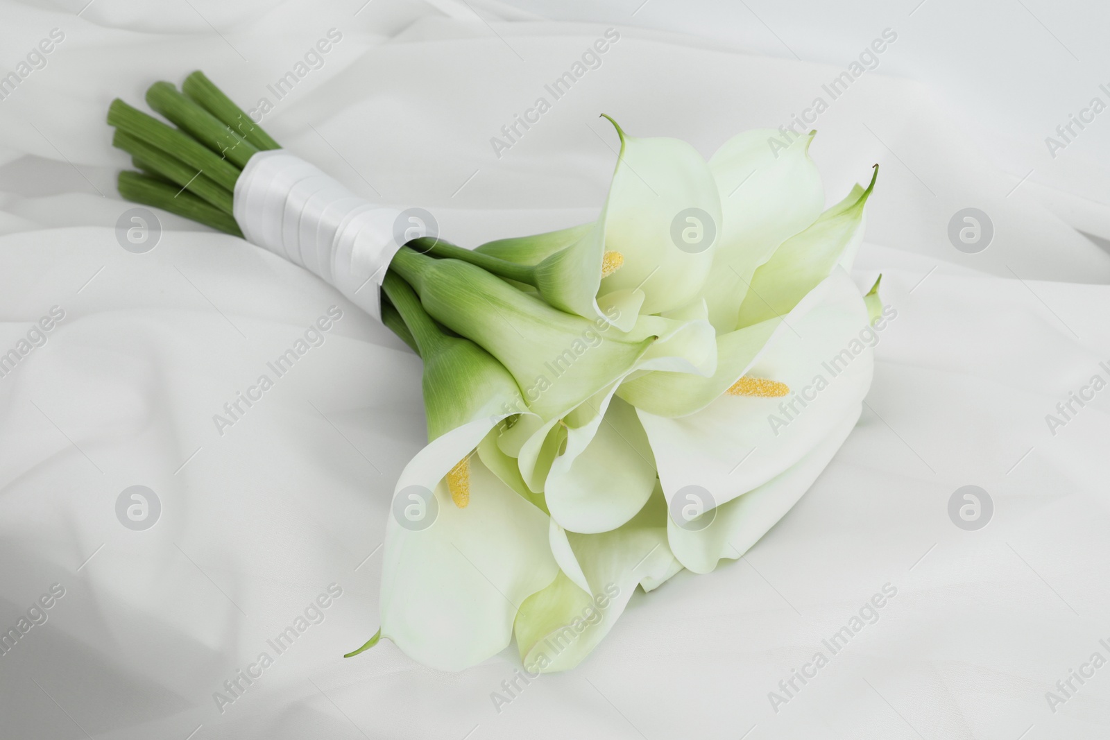Photo of Beautiful calla lily flowers tied with ribbon on white fabric