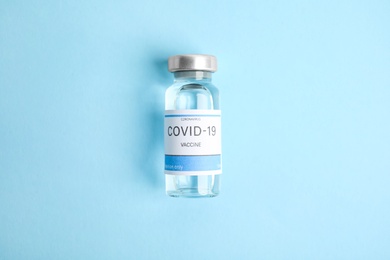 Photo of Vial with coronavirus vaccine on light blue background, top view