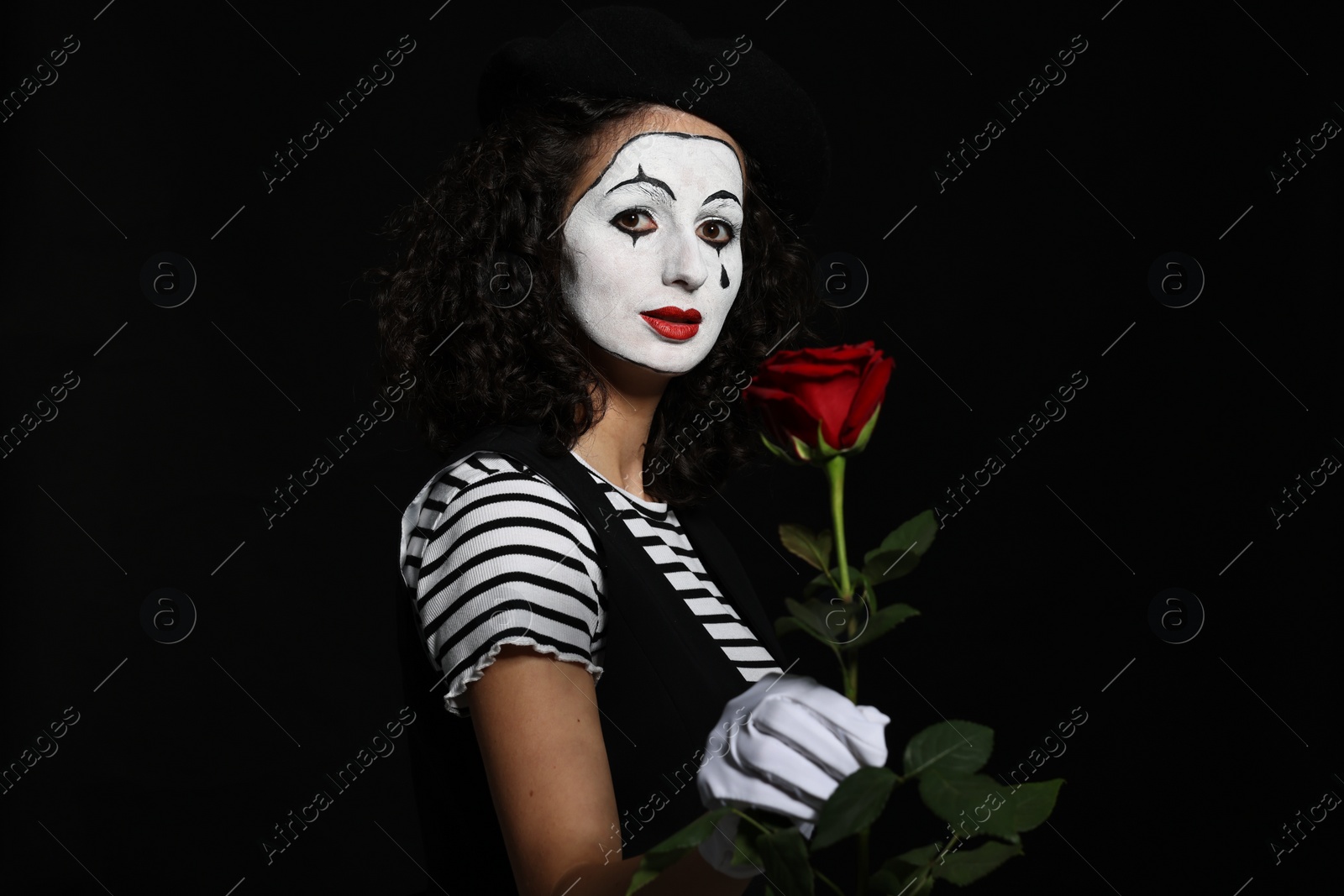 Photo of Young woman in mime costume with red rose posing on black background